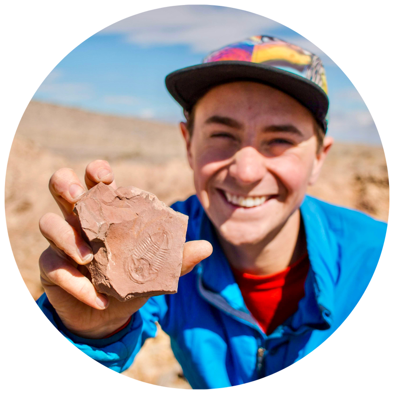 Headshot of Jeremy Snyder, grinning while holding a trilobite fossil